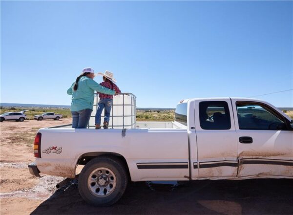 Woman and child standing in truck bed with large water tank.