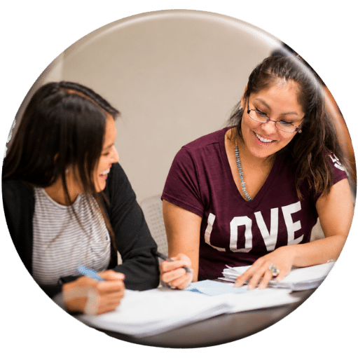 Two smiling women holding pens and collaborating over papers at a study table.